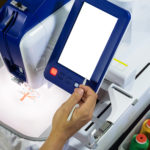 worker's hand is holding stick working with embroidery machines next to colorful threads in plastic box and tool box on the table